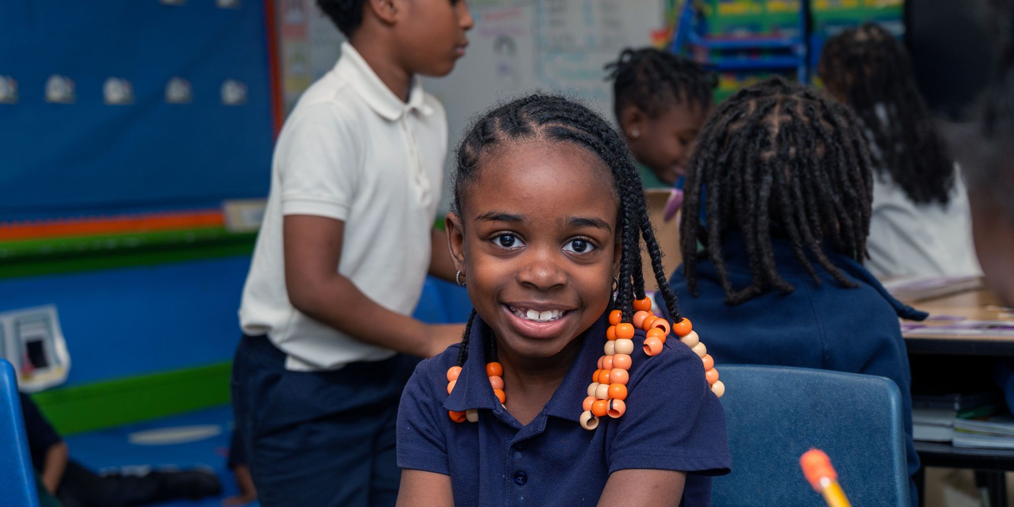 Smiling student with beaded braids in a classroom.