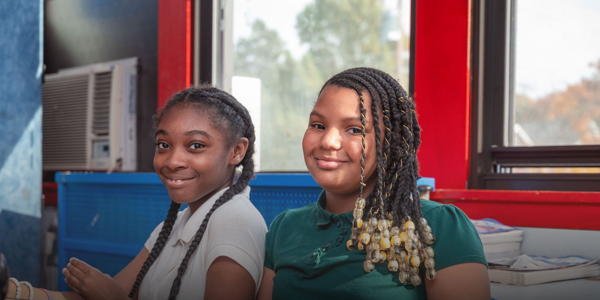 Two smiling students with braided hair in a classroom.